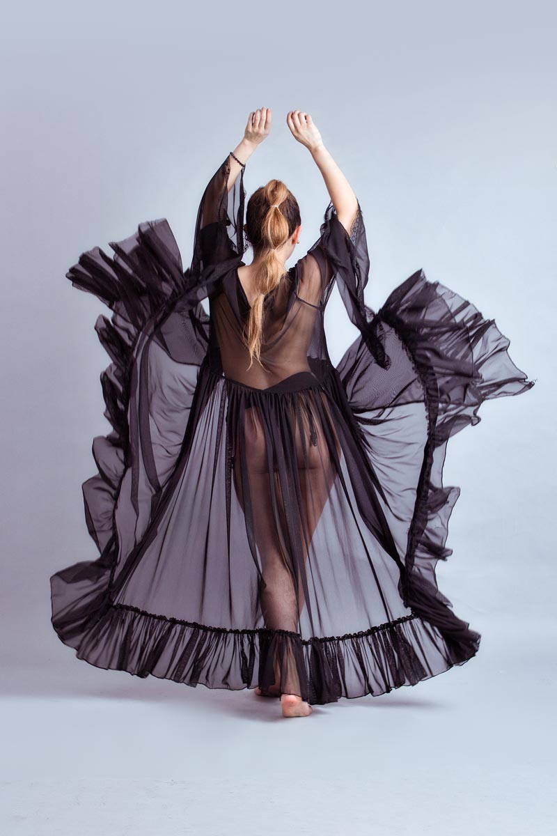 Flor Jesarelt de espaldas con bata negra semitransparente y brazos elevados, tela en movimiento, sesión editorial fashion CDMX, fotografía por Josué Palma