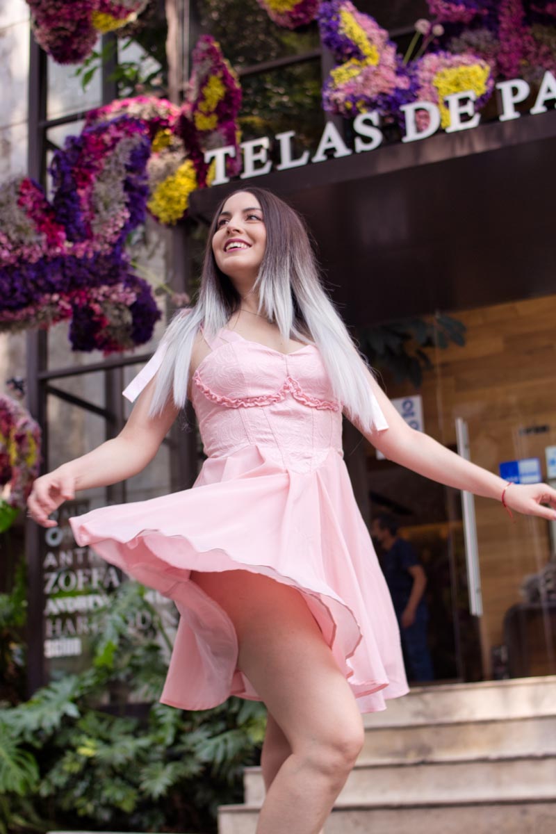 Magali Castagno girando con vestido rosa en ángulo bajo, flores moradas de fondo, sesión de moda editorial en Ciudad de México, fotografía por Josué Palma